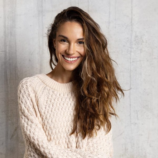 Portrait of cheerful smiling girl. Lovely girl with healthy dark hair posing isolated on beige background in warm sweater. Beauty and winter concept